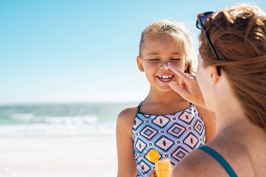 Moving to Portugal - Mother applies sun-tan lotion to her daughters nose at the beach